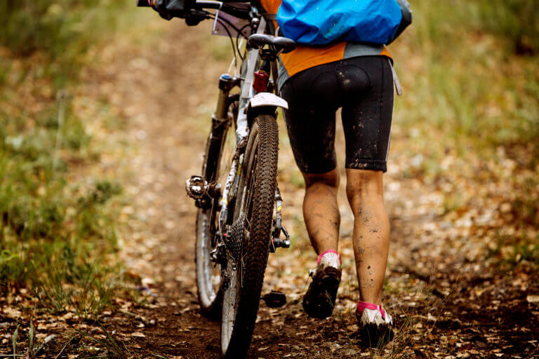 Muddy cyclist walking their mountain bike up a hill