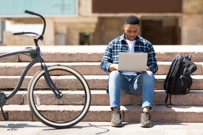 Student using his laptop on the steps next to his backpack and bicycle