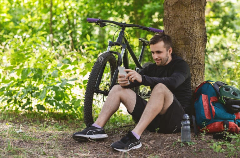 Man sitting near a tree and his bicycle on his phone