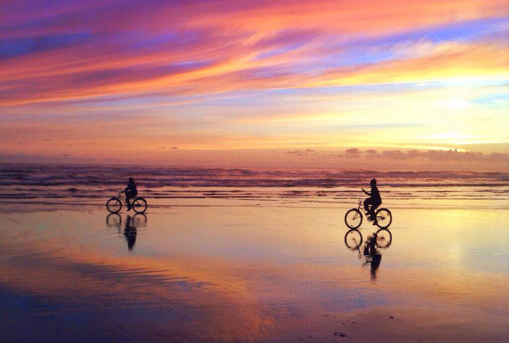 Couple riding their bicycles on the beach at sunset