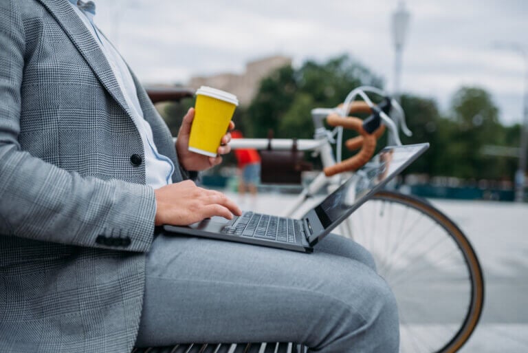 Business man holding a cup of coffee by his bicycle on a bench