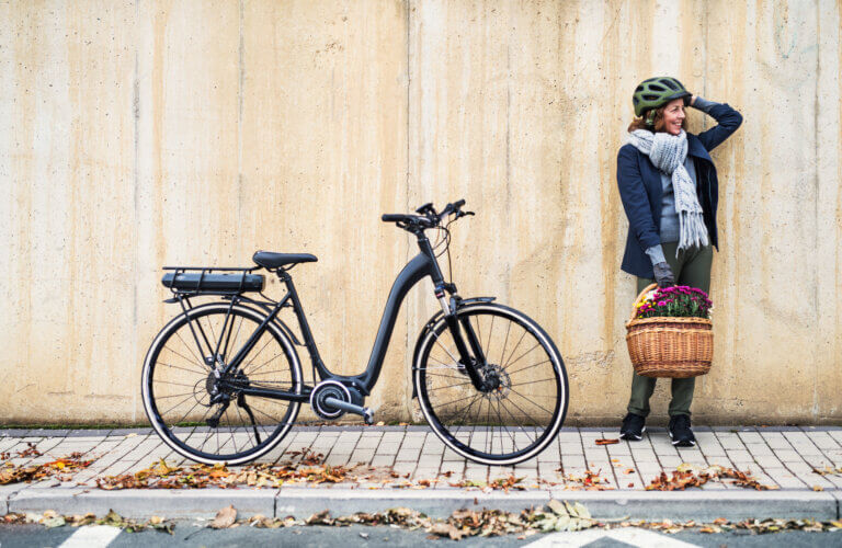 Woman wearing bicycle helmet holding a basket and standing next to her bicycle