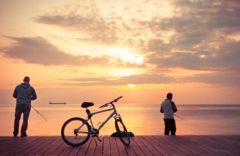 Two men fishing on a dock behind a bicycle