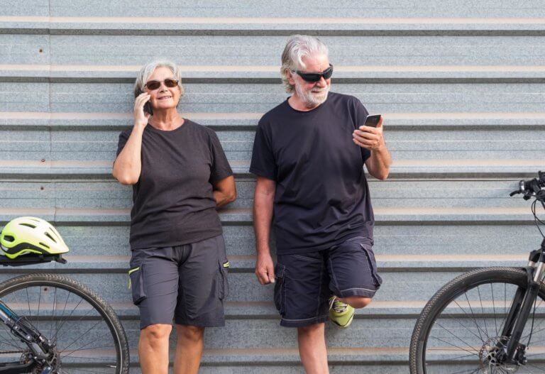 Smiling senior couple standing against a garage door with their electric bicycles
